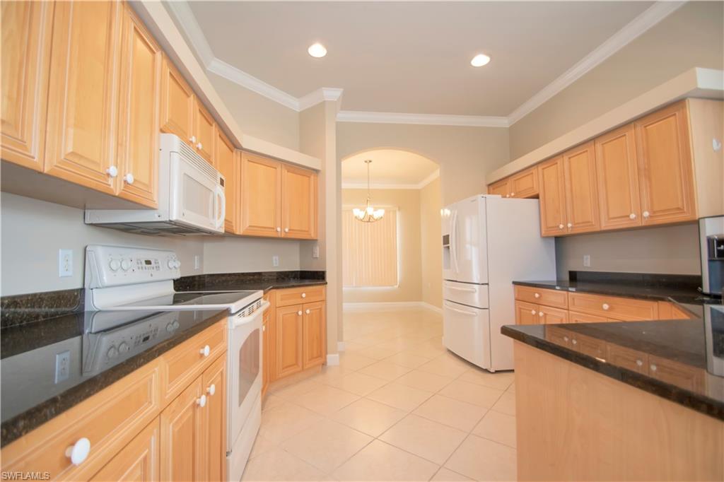 Kitchen with a notable chandelier, white appliances, light tile patterned floors, decorative light fixtures, and ornamental molding