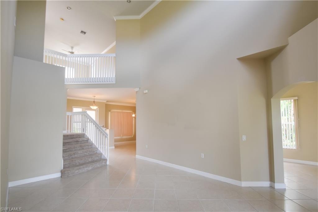 Tiled empty room with crown molding and a high ceiling