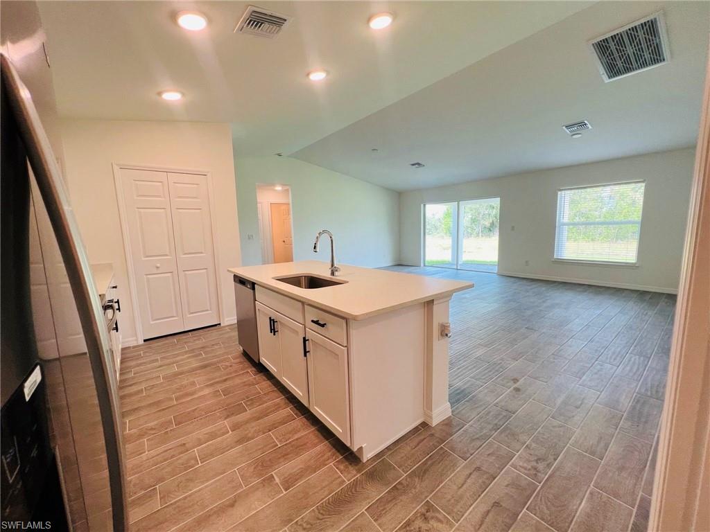 Open-concept kitchen featuring a center island with sink and integrated dishwasher, wood-finish flooring, recessed lighting, and white cabinetry with dark hardware