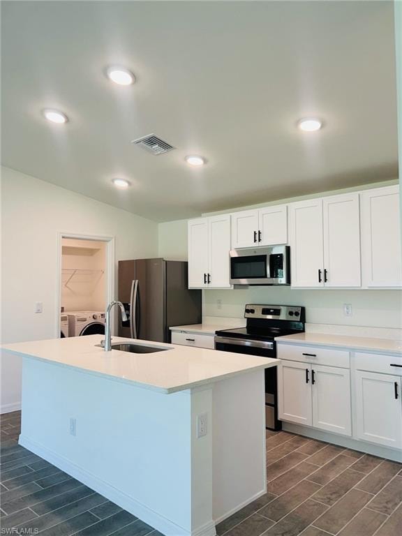 Modern kitchen featuring a central island with an undermount sink, white cabinetry, stainless steel appliances, and quartz countertops