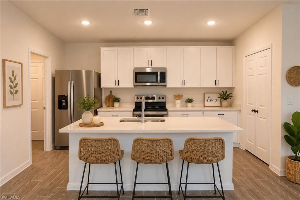 Modern kitchen featuring a central island, white cabinetry with matte black hardware, stainless steel appliances, light-toned countertops, and wood-finish flooring