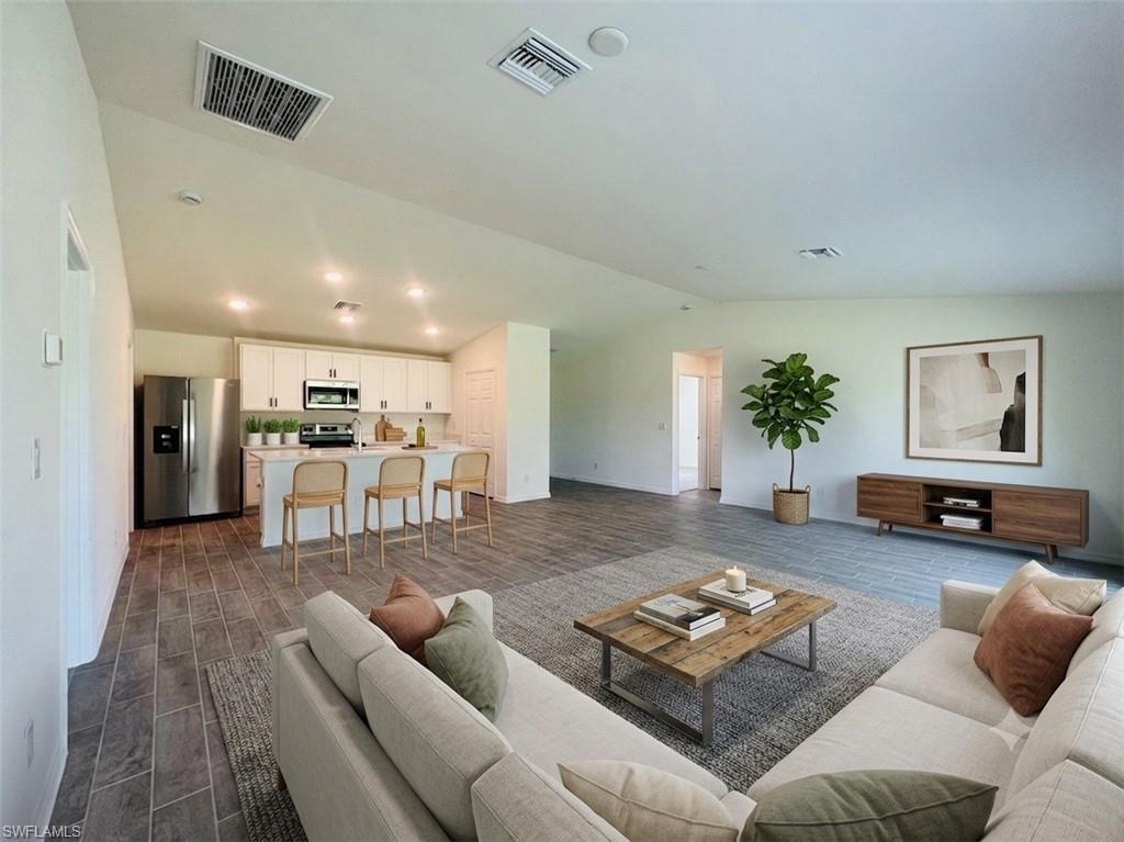 Open-concept living area featuring wood-finish flooring, recessed lighting, and a white kitchen with stainless steel appliances