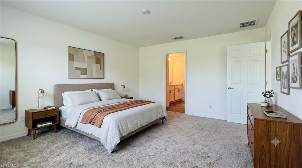 Spacious bedroom featuring plush carpeting, a multi-panel interior door, and an entryway to a full bathroom with a vanity