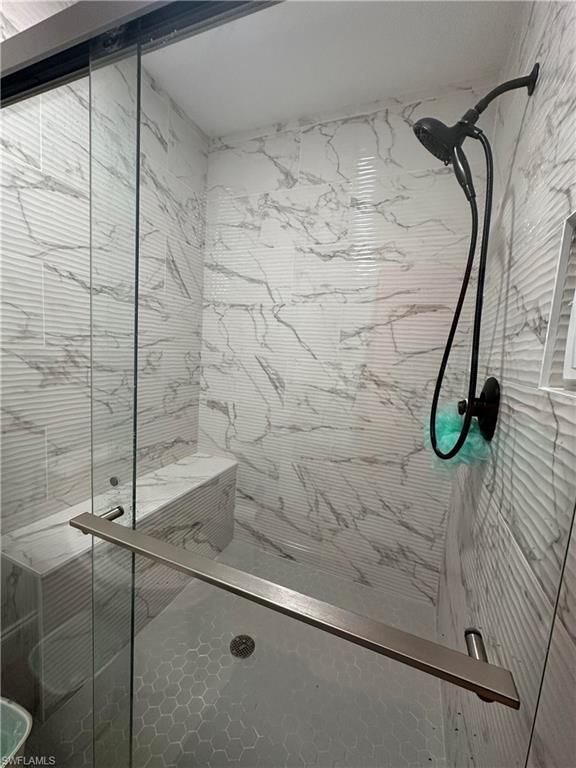 Glass-enclosed shower featuring a built-in bench, hexagonal floor tiles, and a matte black shower fixture