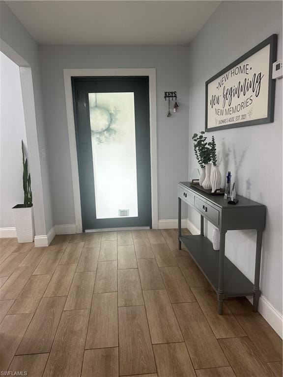 Entryway featuring wood-finish tile flooring, a dark-paneled door with a frosted glass insert, and crisp white baseboards