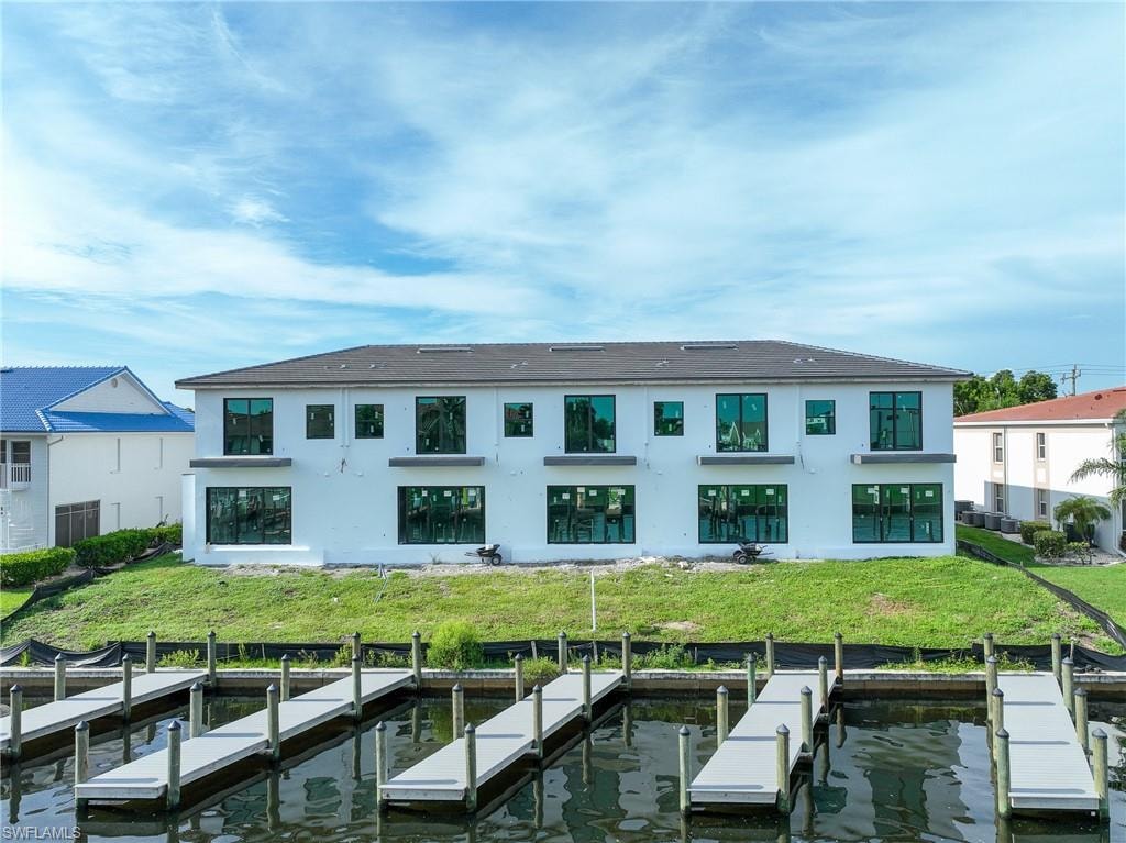 Waterfront residence with multiple private boat slips, featuring a two-story structure, expansive glass windows, and a black shingle roof