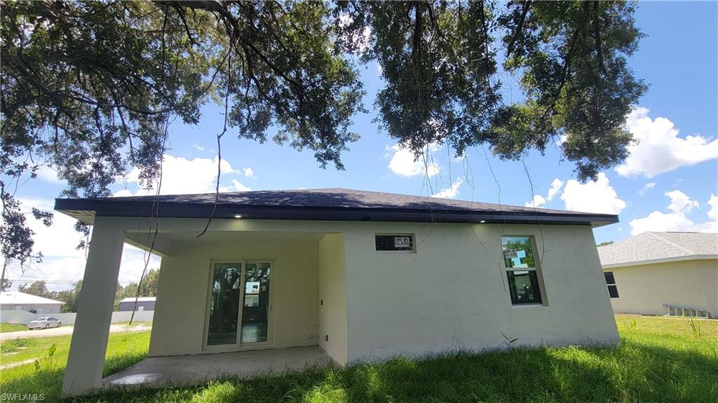 Rear exterior featuring a covered patio, sliding glass doors, white stucco finish, and a dark shingle roof