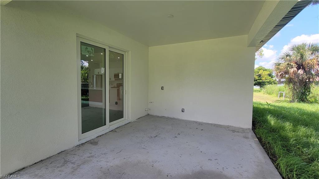 Covered concrete patio with sliding glass doors and access to an exterior green space