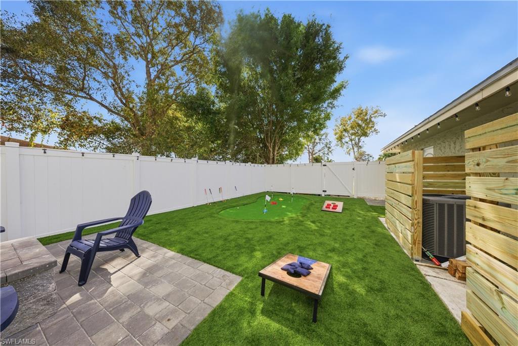 Private backyard featuring a paved patio, artificial turf, putting green, and white privacy fencing