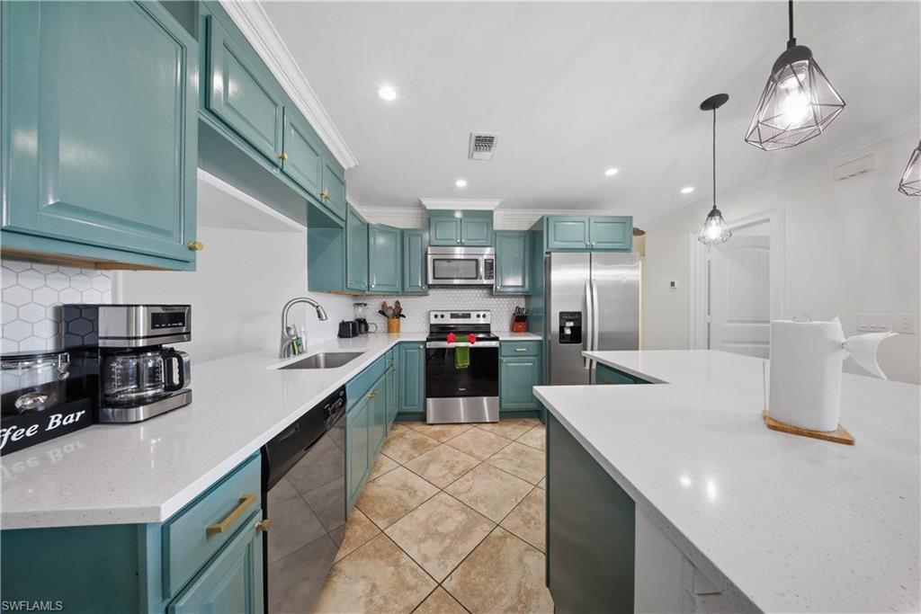 Modern kitchen featuring teal cabinetry, white countertops, stainless steel appliances, a hexagonal tile backsplash, and recessed lighting