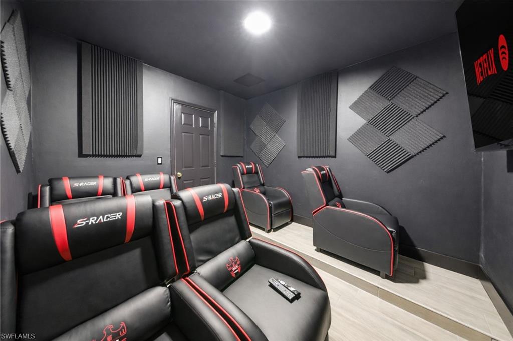Dedicated media room featuring multi-level seating, wall-mounted acoustic panels, wood-finish flooring, and a dark paneled door