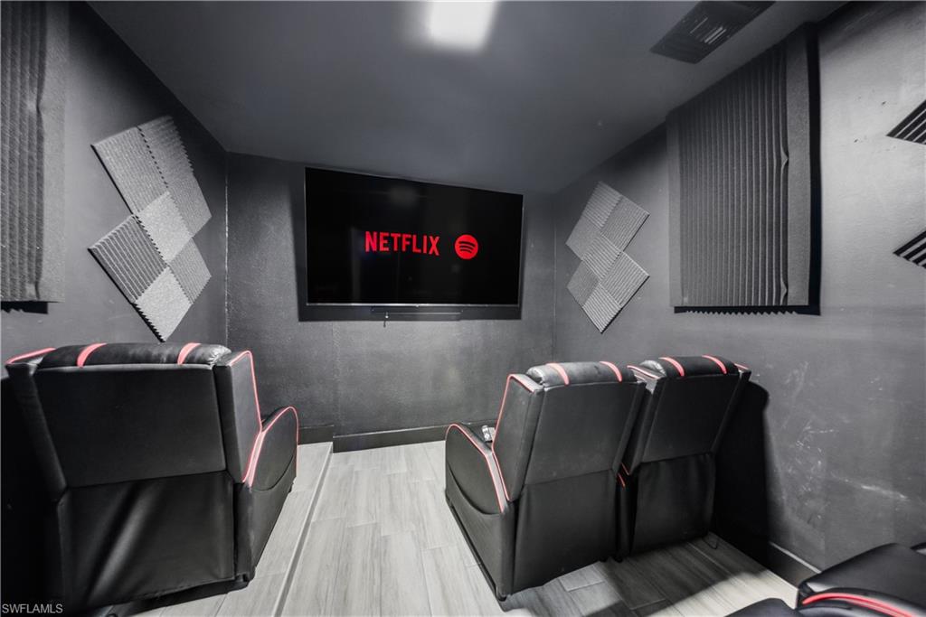Dedicated media room featuring a wall-mounted flat-screen display, acoustic wall paneling, light wood-finish flooring, and recessed ceiling lighting