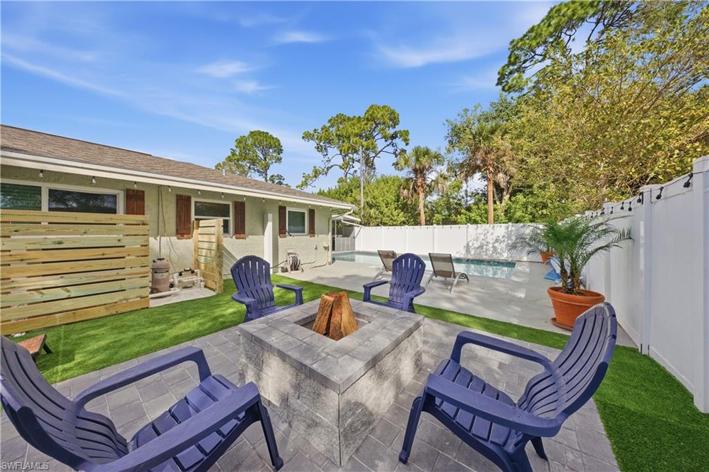 Paver patio with a built-in stone fire pit, surrounding artificial turf, a privacy fence, and an in-ground pool