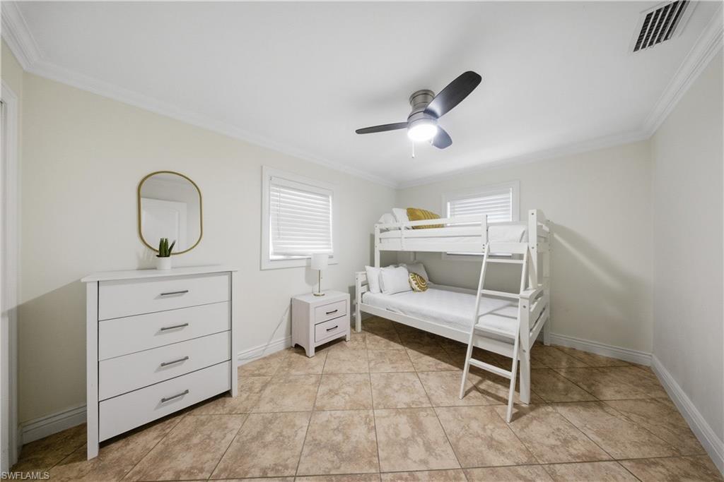Spacious room featuring tile flooring, white walls, crown molding, and a ceiling fan with integrated lighting