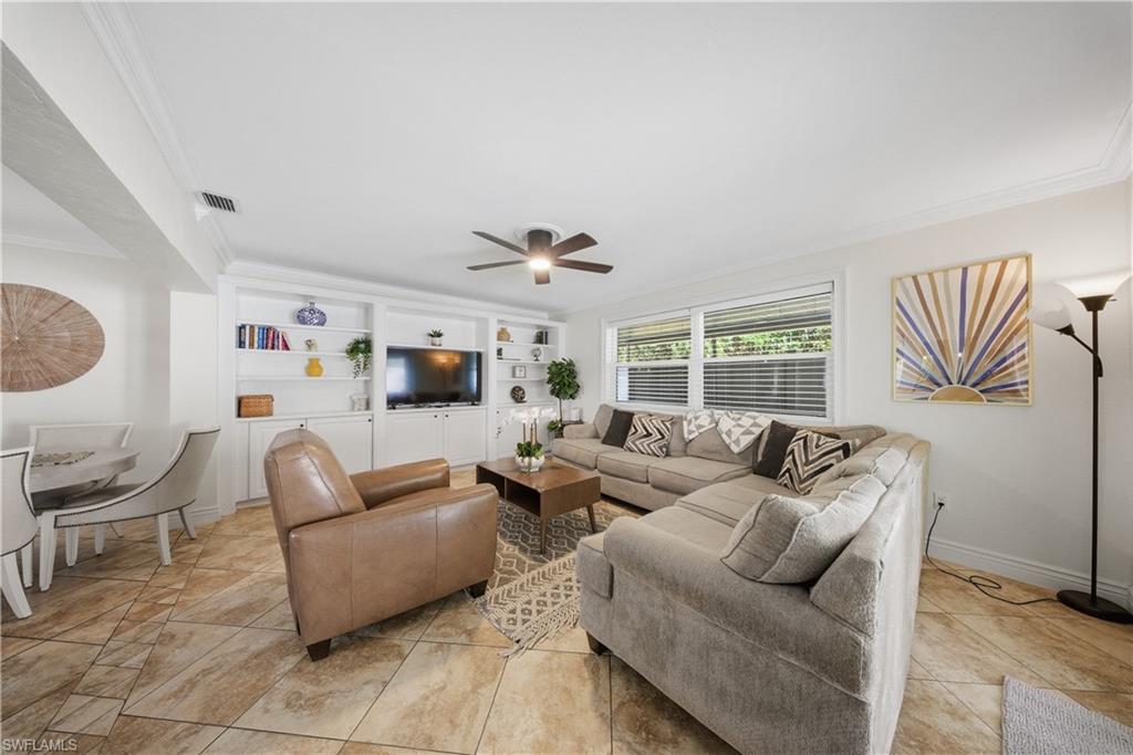 Living room featuring tile flooring, built-in shelving, white trim, a ceiling fan, and multiple windows with blinds