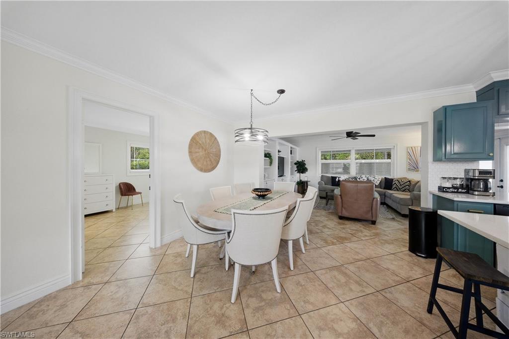 Dining area featuring neutral-toned tile flooring, crown molding, and an overhead pendant light fixture
