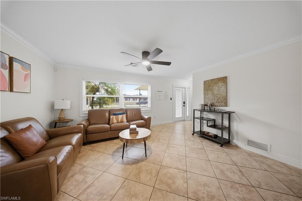 Living area featuring diagonal tile flooring, crown molding, a ceiling fan, and large windows with blinds