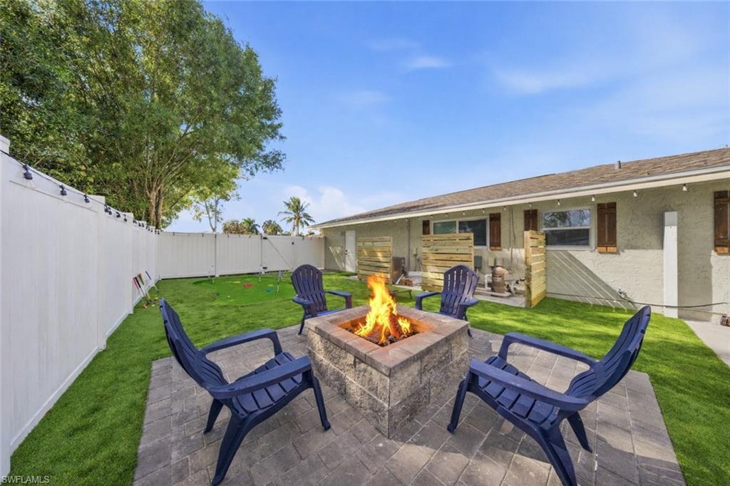 Backyard featuring a paver patio with a built-in stone fire pit, surrounded by a white vinyl privacy fence and manicured lawn