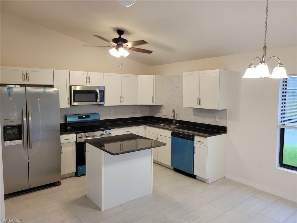 Kitchen with ceiling fan with notable chandelier, stainless steel appliances, a center island, hanging light fixtures, and lofted ceiling