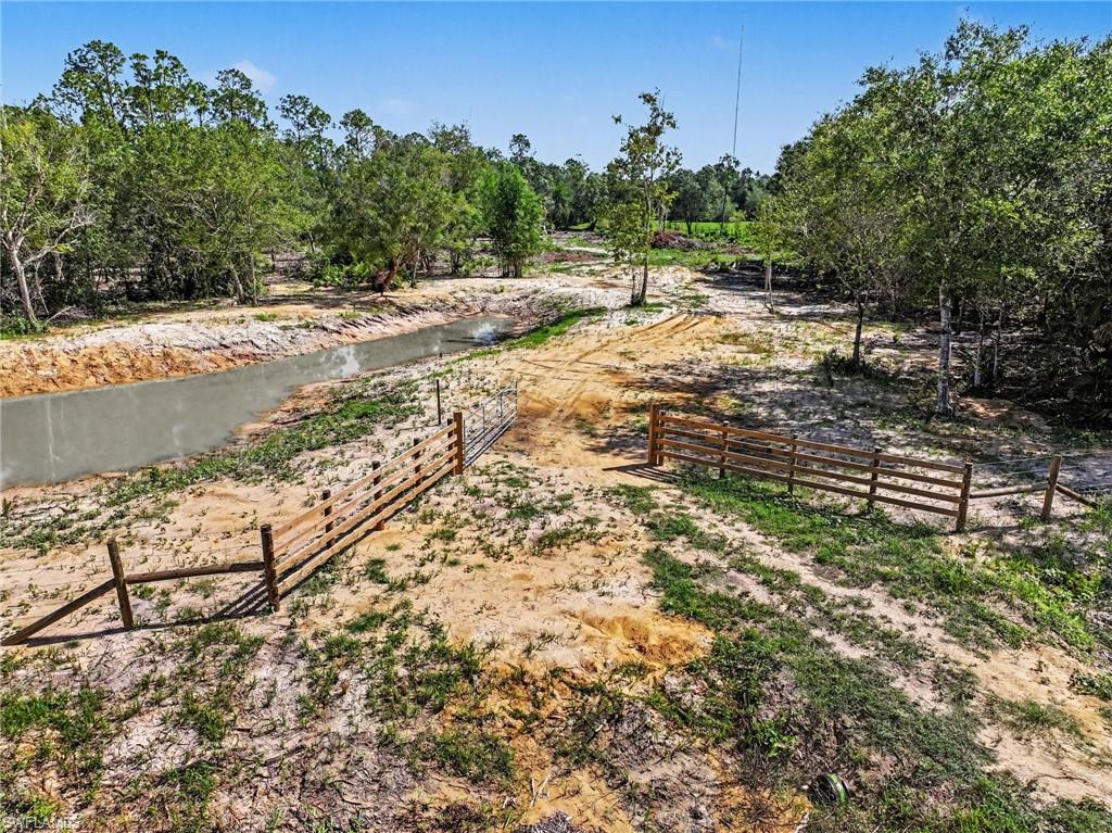 Expansive land parcel featuring a pond and wooden fencing at the entry, and established trees