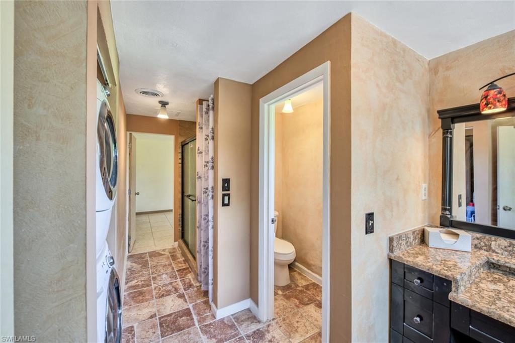 Bathroom with vanity, walk in shower, toilet, and stacked washer / dryer