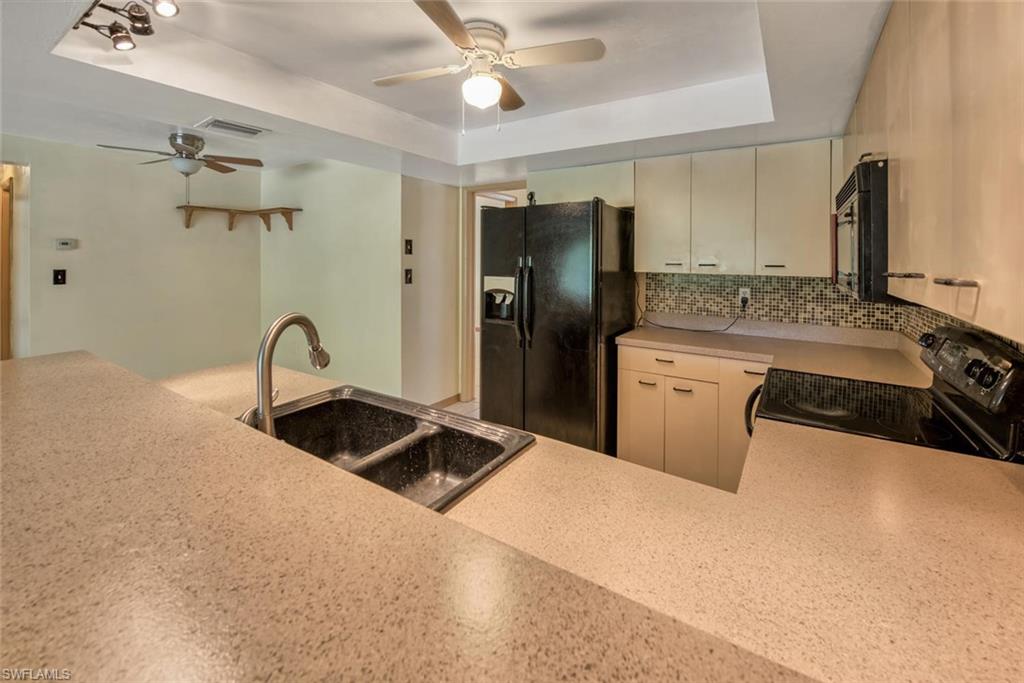 Kitchen with sink, black appliances, a raised ceiling, decorative backsplash, and cream cabinetry