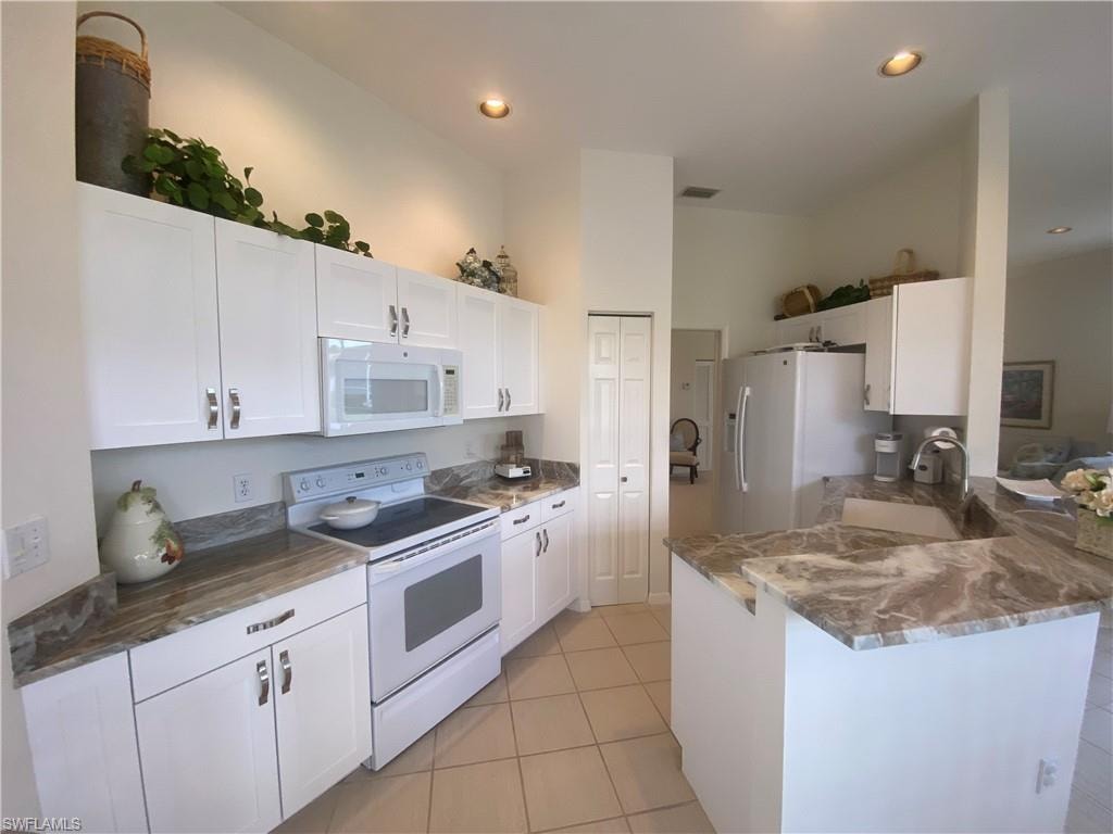 Kitchen with white cabinetry, light tile patterned floors, a peninsula, and white appliances