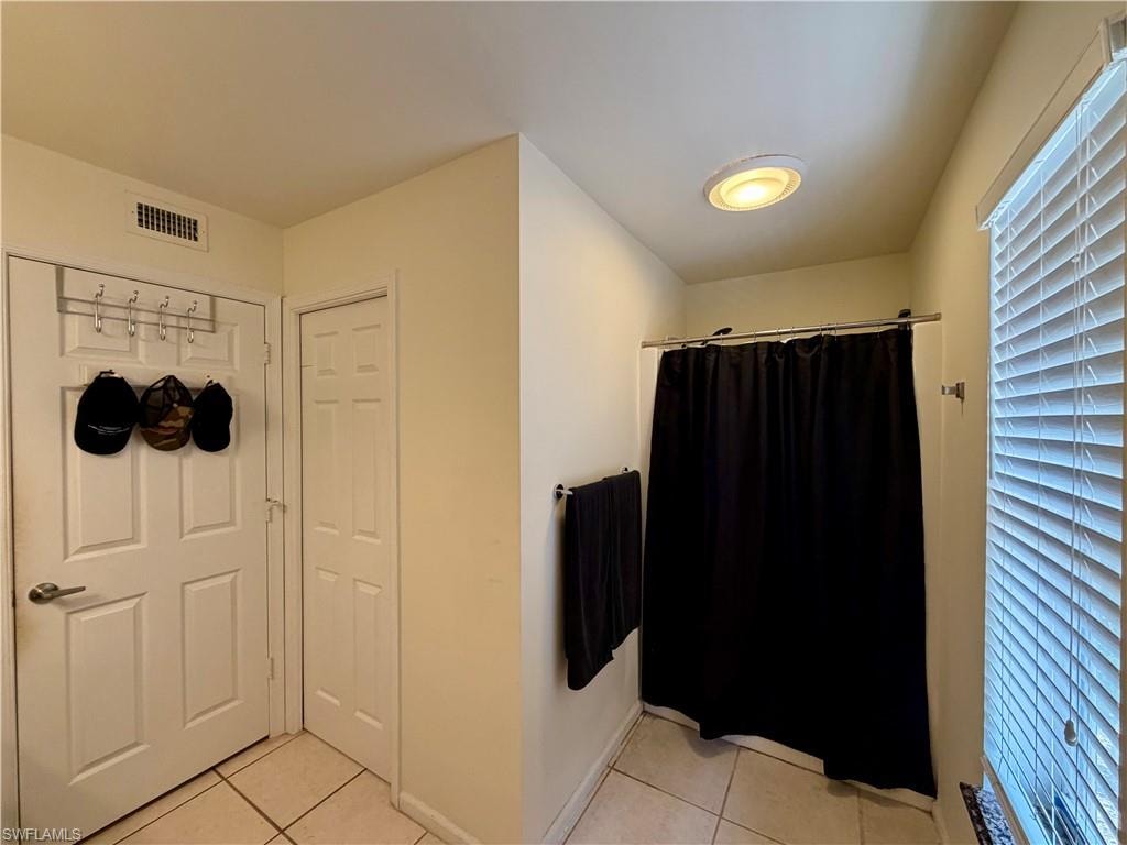Full bathroom featuring a shower stall with black curtain, ceiling-mounted light fixture, white blinds, and light-toned floor tiling