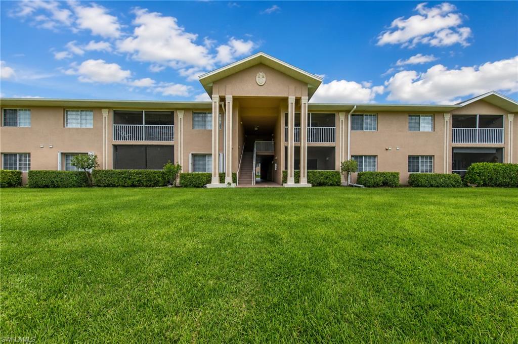 Two-story residential building featuring a central portico entrance with columns, multiple screened balconies, and a manicured lawn
