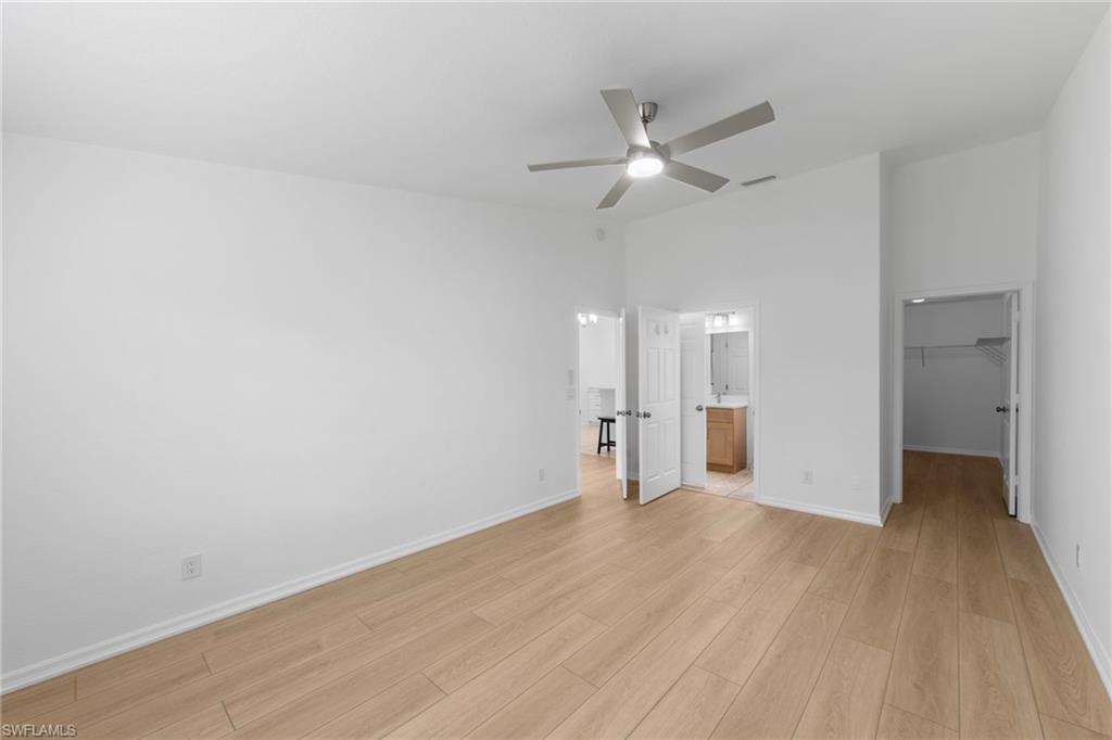 Spacious room featuring wood-finish flooring, a modern ceiling fan, and crisp white walls