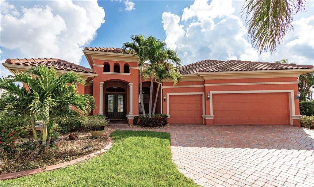 Mediterranean-style exterior featuring a tile roof, stucco finish, paver driveway, arched entryway, and mature landscaping