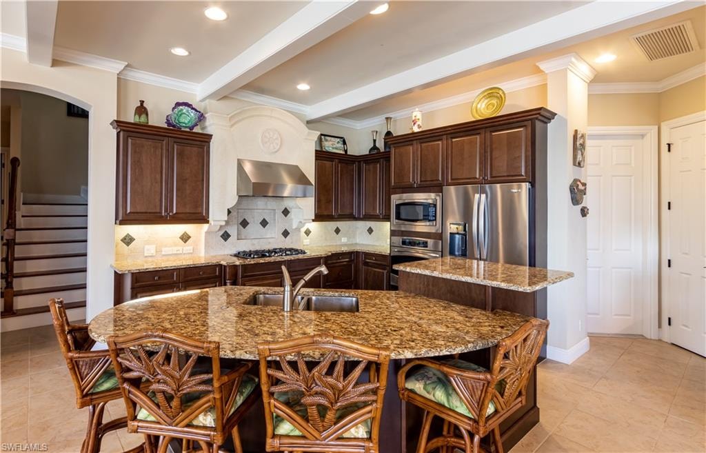 Gourmet kitchen featuring a large granite-topped island with an undermount sink, rich wood cabinetry, stainless steel appliances, a tiled backsplash, and recessed lighting