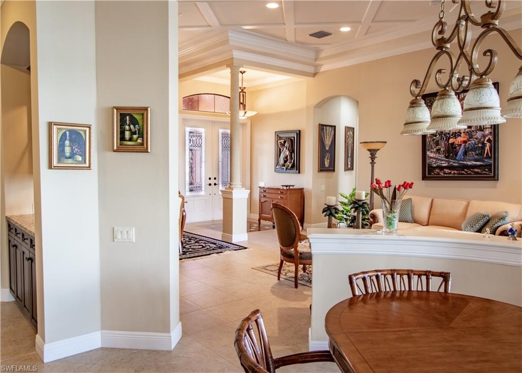 Spacious interior featuring a coffered ceiling, tile flooring, an ornate chandelier, arched doorways, and a built-in wet bar with a granite-look countertop
