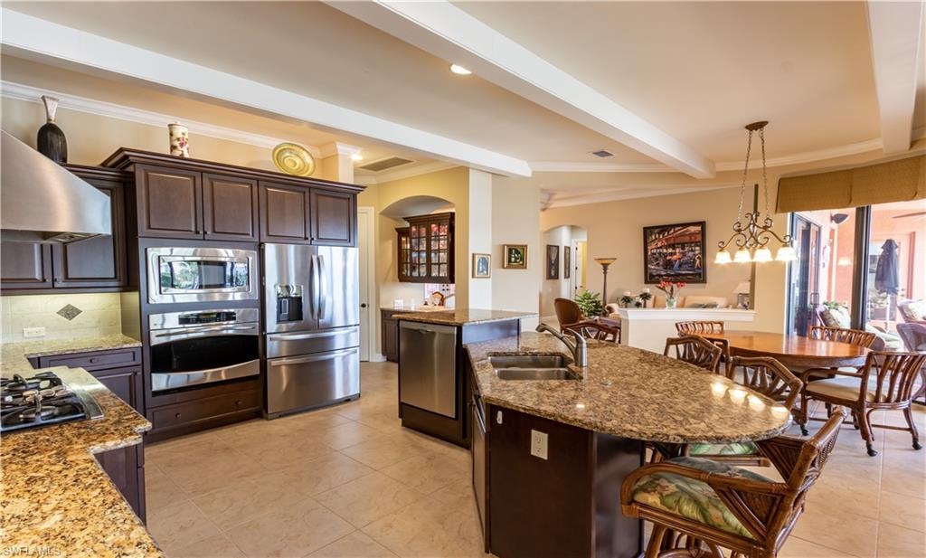Gourmet kitchen with stainless steel appliances, dark wood cabinetry, granite countertops, and a central island featuring a double-basin sink