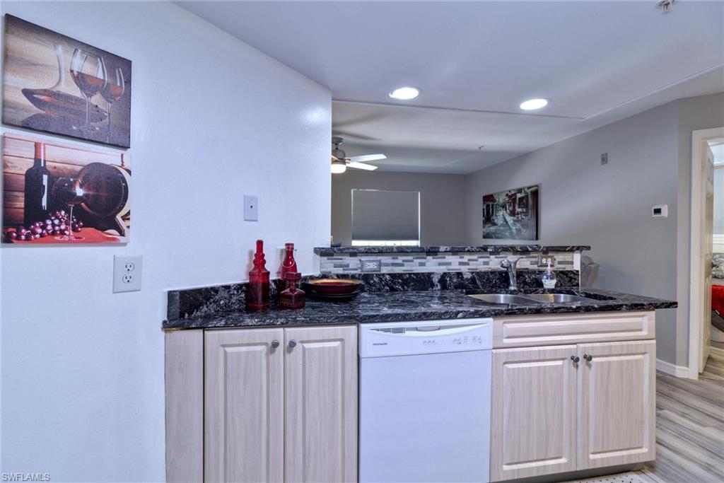 Kitchen with dishwasher, dark stone countertops, light hardwood / wood-style floors, sink, and backsplash