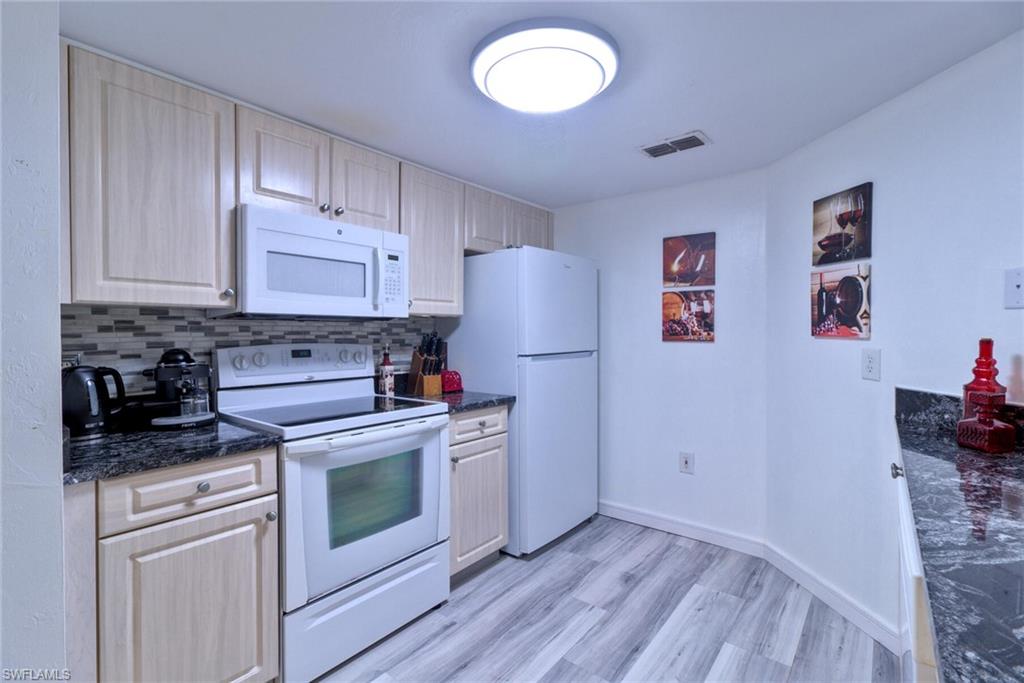 Kitchen with white appliances, light brown cabinets, dark stone countertops, decorative backsplash, and light wood-type flooring