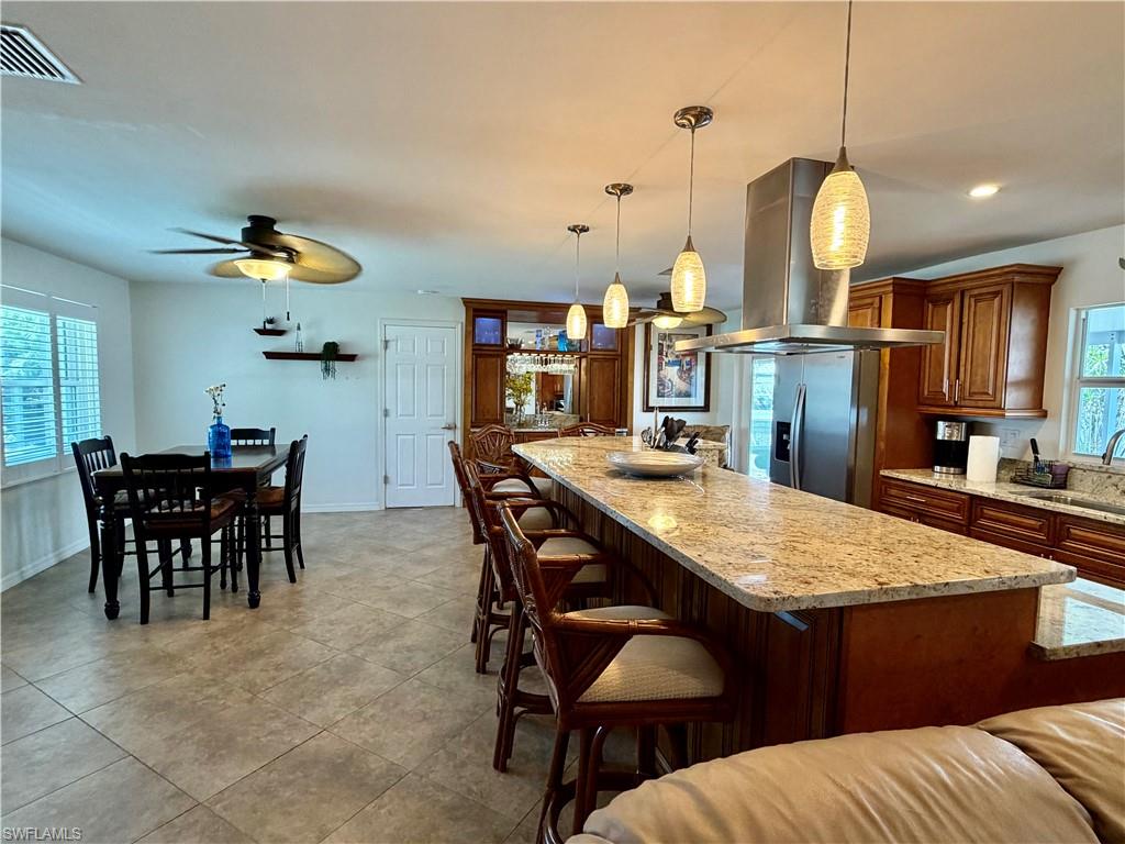 Open-concept kitchen and dining area featuring a large island with stone countertops, pendant lighting, stainless steel appliances, wood cabinetry, and tile flooring
