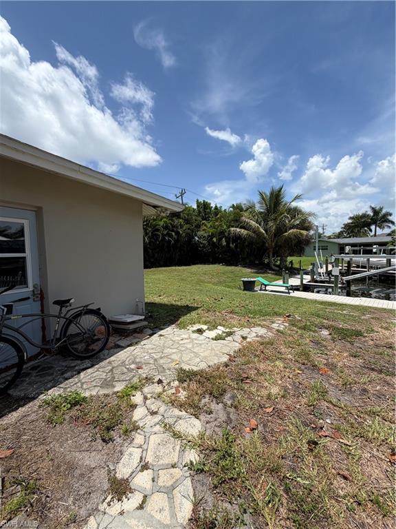 Waterfront property featuring a grassy expanse, mature palm trees, and a stone-patterned pathway