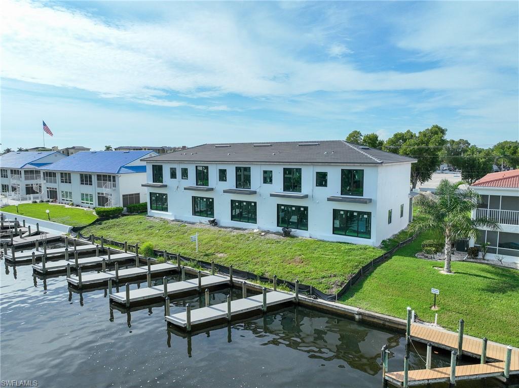 Modern waterfront residence featuring a clean-lined white exterior with expansive multi-pane windows, manicured lawn sloping toward the water's edge, and direct private dock access with multiple boat slips
