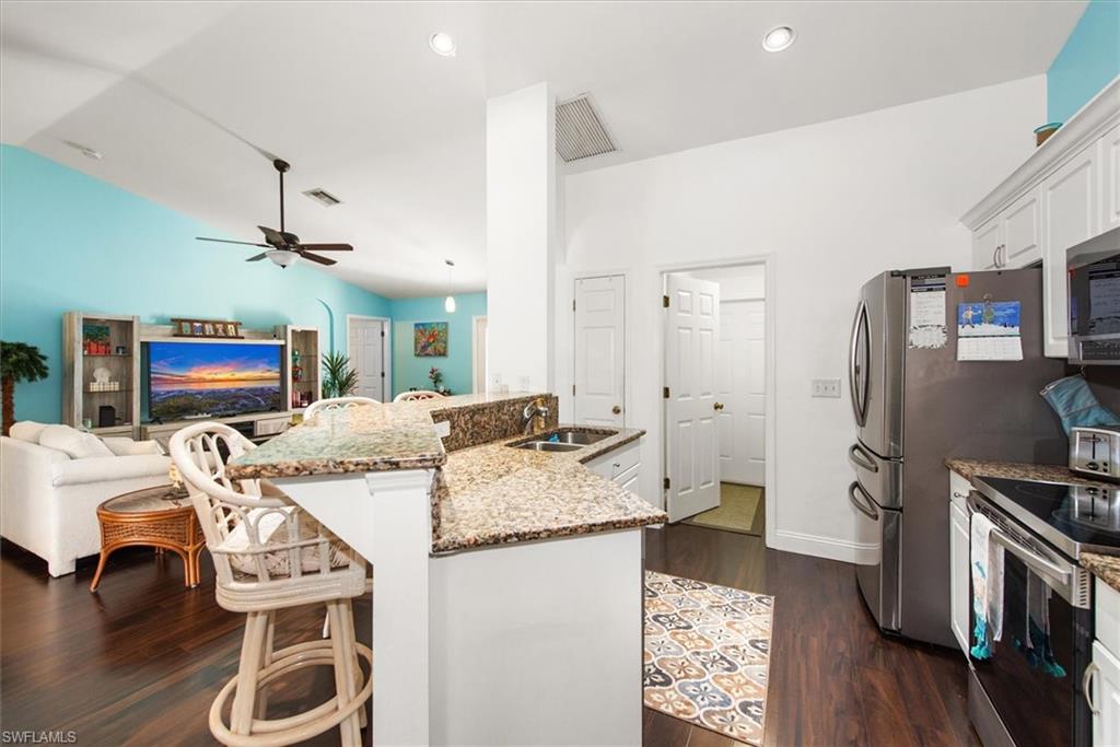 Open concept kitchen featuring granite countertops, a double basin sink, stainless steel appliances, and white cabinetry