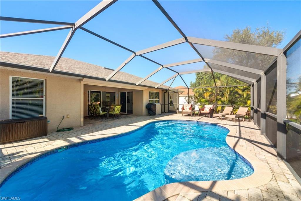 Screened outdoor living area featuring a free-form swimming pool with integrated spa, paver decking, and direct access to the interior through sliding glass doors