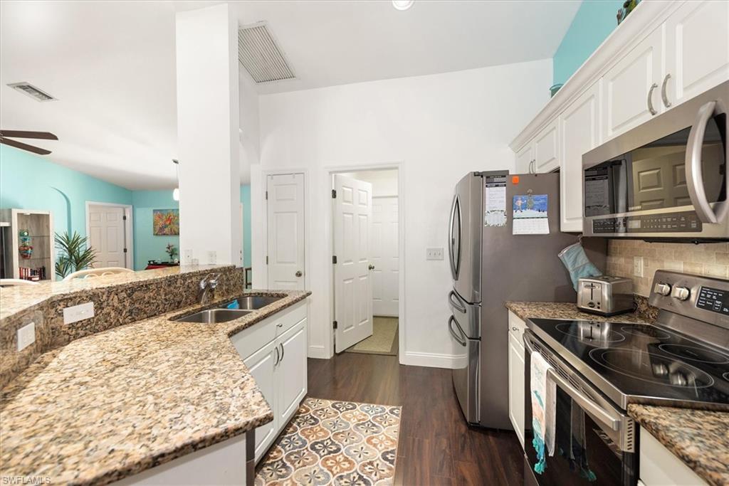 Kitchen featuring stainless steel appliances, granite countertops, white cabinetry, dark wood-finish flooring, and a double basin sink