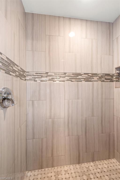 Tiled shower enclosure featuring light-toned large format wall tiles, a decorative mosaic accent band, and a mosaic tile shower floor