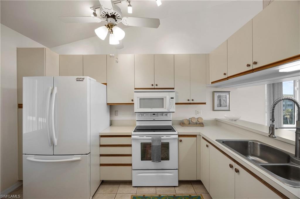 Kitchen featuring white appliances, light countertops, cream cabinets, light tile patterned flooring, and vaulted ceiling