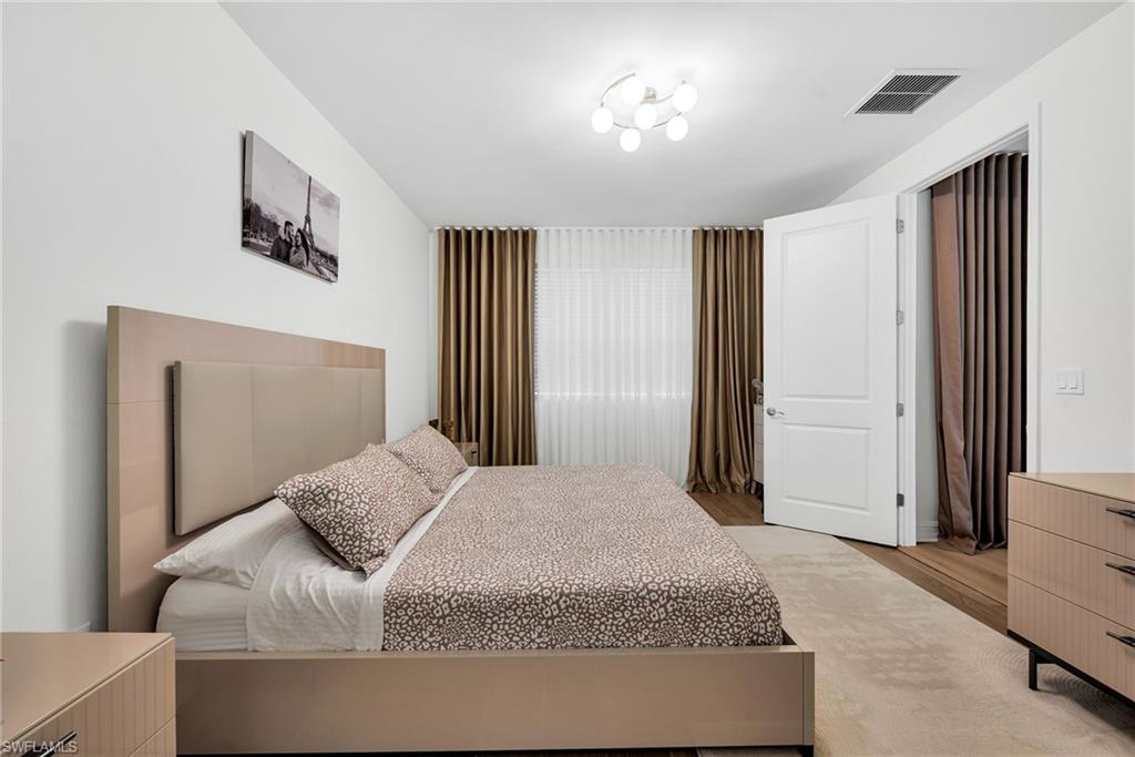 Spacious bedroom featuring light neutral wall paint, a modern ceiling light fixture, and a large window with sheer and blackout drapery