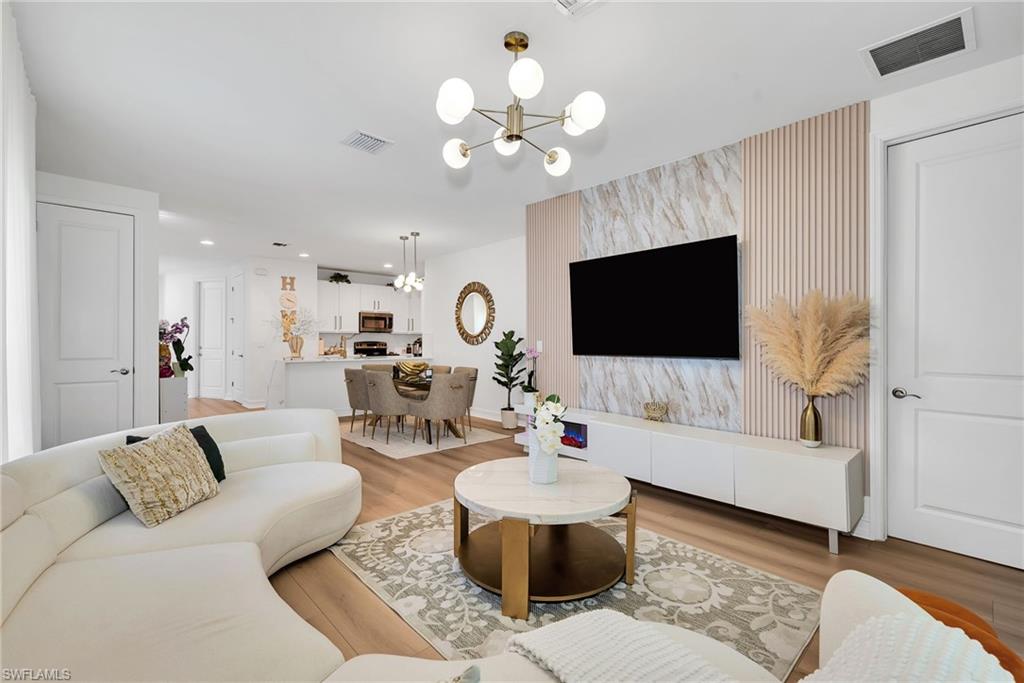 Open-concept living space featuring wood-finish flooring, a contemporary chandelier, and a decorative accent wall with vertical paneling and a stone-look panel