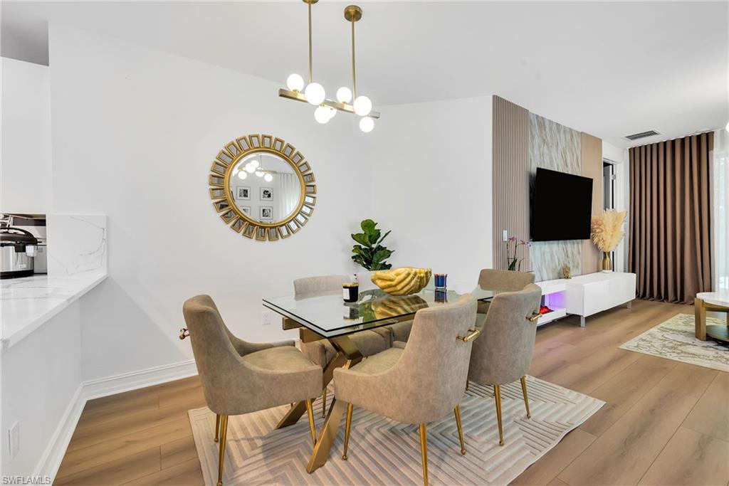 Open-concept living space featuring wood-finish flooring, a contemporary dining area with a glass-top table, and a media wall with decorative paneling