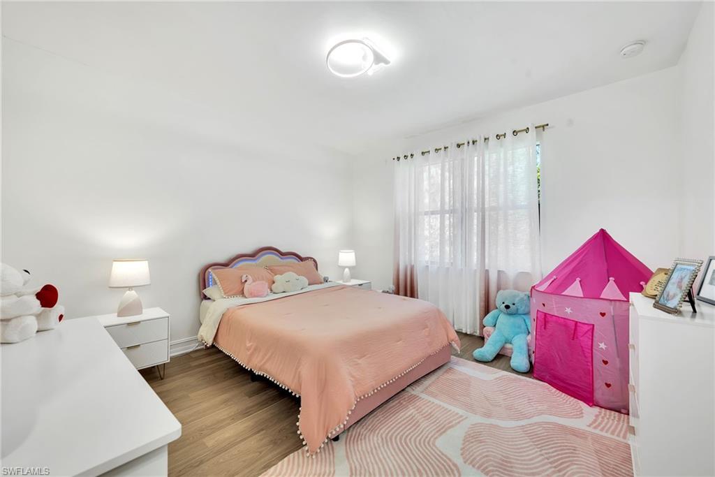 Room featuring wood-finish flooring, white walls, and a large window with sheer white curtains