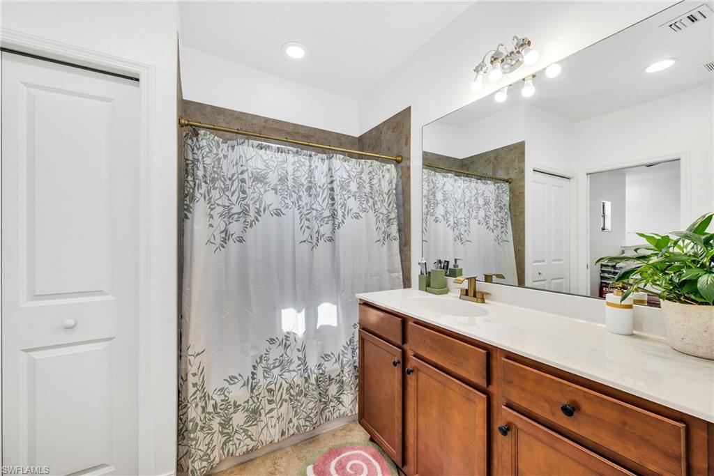Bathroom featuring a wood-finish vanity with a single basin, a large mirror, and recessed lighting