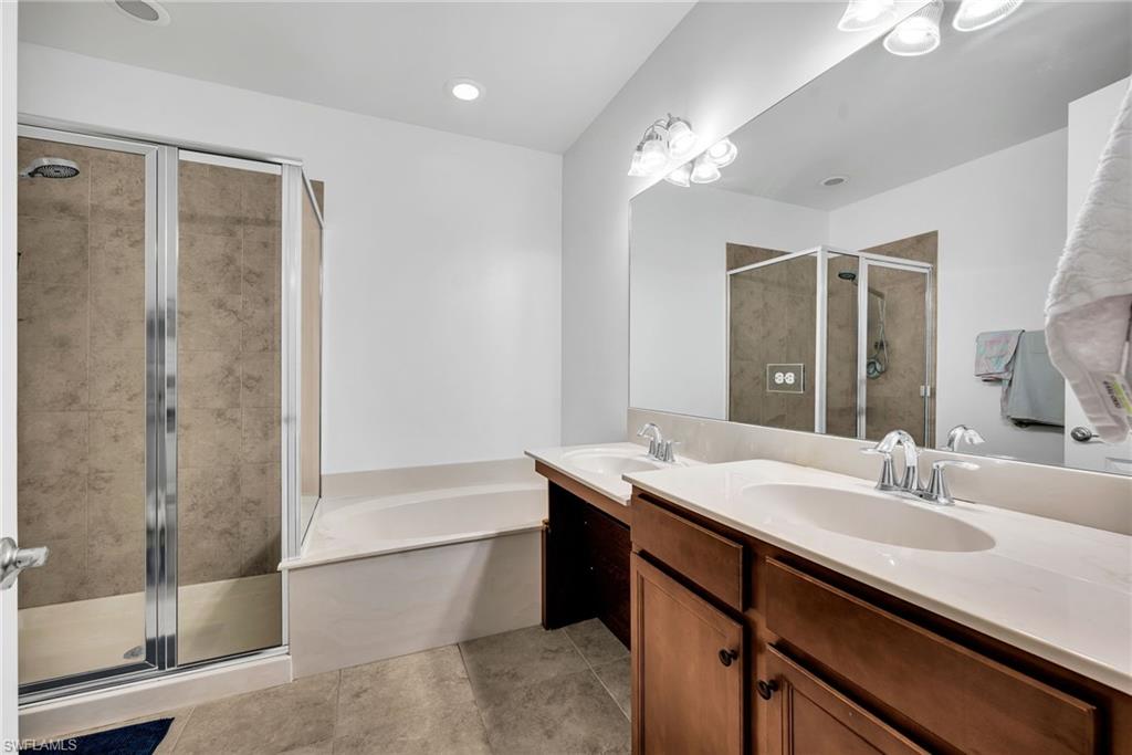 Bathroom featuring a glass-enclosed shower with tile surround, separate soaking tub, and a dual vanity with light-colored countertops